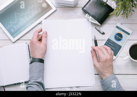 Man holds a piece of paper with empty space for your text. Tablet and smartphone over the desk with application maded in graphic program. Stock Photo