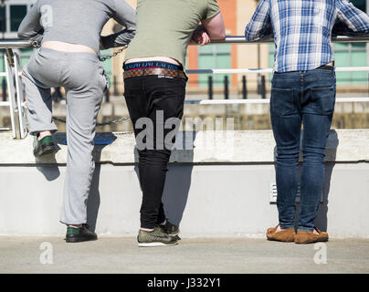 Rear view of three young men leaning on railing in UK city centre Stock Photo