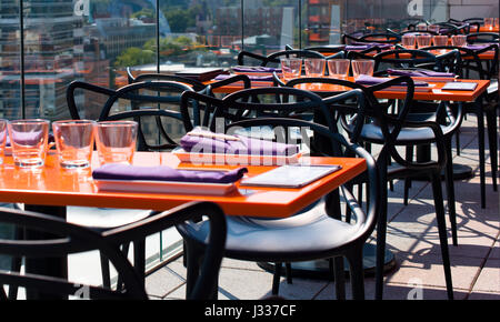 Interior of a modern restaurant with modern orange rectangular tables and chairs and a stylish serving in the attic outdoors behind a glass barrier Stock Photo