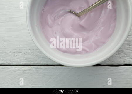 Creamy naturally colored rasberry fruit yogurt in white glass bowl on white wood plank table close up with spoon -  top view photograph Stock Photo