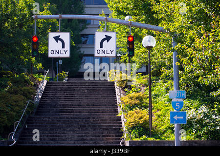 Two traffic lights with a red light on a pole with travel direction arrow in opposite directions. Against the background of a pointer to the road Stock Photo