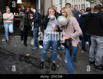 Young people on the streets of London taking legal highs, sniffing nitrous oxide inhaled in balloons, Tower Bridge, London, UK Stock Photo