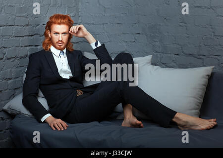 Stylish man in a suit with freckles on his face and beard. The business suit lying on the bed. Stock Photo