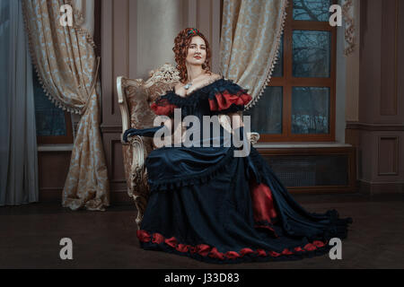 Woman in Victorian dress sitting on a chair in the room. Stock Photo