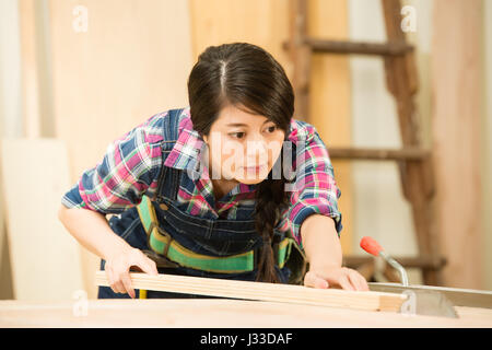 Skilled carpenter cutting a piece of wood in her woodwork workshop, using a circular saw. mixed race asian chinese model. Stock Photo