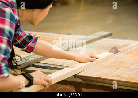 woman carpenter working on an electric buzz saw cutting some boards wearing smartwatch. mixed race asian chinese model. Stock Photo