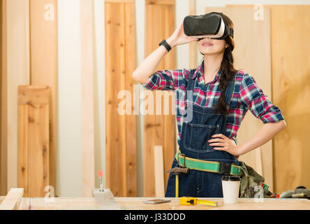 Artisan woodwork studio with shelving holding pieces of wood, with a carpenter standing in his workshop experience using a VR glasses device. mixed ra Stock Photo