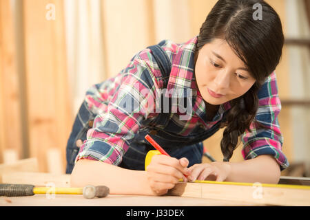 Close-up of craftsman hands in measuring wooden plank with ruler and pencil. Woodwork and renovation concept. mixed race asian chinese model. Stock Photo