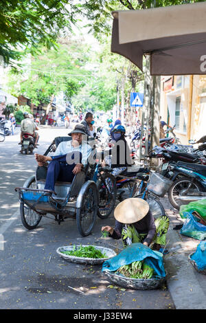 NHA TRANG, VIETNAM - JANUARY 20: Vietnamese woman in traditional conical hat is sorting greens on the street of Nha Trang on January 20, 2016 in Nha T Stock Photo