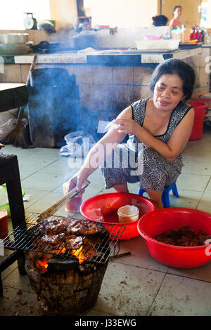 NHA TRANG, VIETNAM - JANUARY 20: Woman is cooking meat on the fire at the vietnamese style food court on January 20, 2016 in Nha Trang, Vietnam. Stock Photo