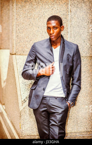 African American teenage boy wearing black fashionable jacket, white undershirt, standing against column outside in New York, innocently looking at yo Stock Photo