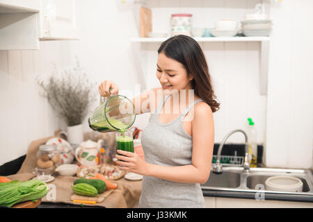 Smiling asian woman making smoothie with fresh vegetables in the blender in kitchen at home. Stock Photo