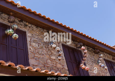 Horizontal shot of upper floor of beautiful old stone house with dark brown wooden window shuttres and several traditional turkish hanging mosaiс lant Stock Photo