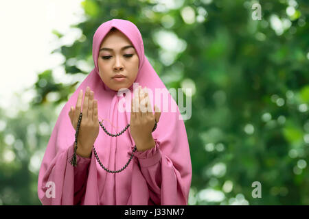 Portrait of asian muslim woman in hijab dress praying to god with blurred background Stock Photo