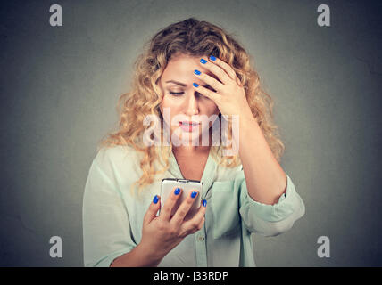 Upset stressed woman holding cellphone disgusted with message she received isolated on gray background. Human face expression emotion feeling reaction