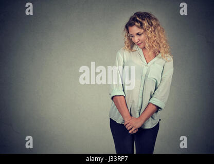 Shy insecure young woman looking down avoiding eye contact standing isolated on gray wall background Stock Photo