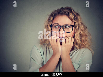 Closeup portrait nervous stressed young woman biting fingernails looking anxiously craving isolated gray background. Human emotion face expression fee Stock Photo