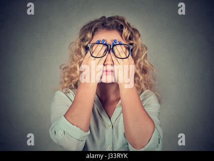 Closeup portrait young woman in glasses covering face eyes using her both hands isolated on gray wall background Stock Photo