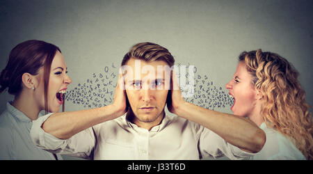 Two young women screaming at a calm man covering his ears with hands ignoring them. Anger management emotional intelligence concept. Love triangle. Ne Stock Photo