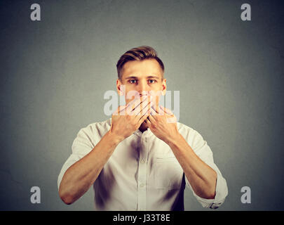 man with hands over his mouth, speechless isolated on gray wall background Stock Photo