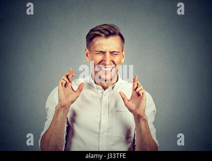 young guy, business man crossing fingers, wishing, hoping for best, miracle isolated on gray background. Human emotion facial expression feeling attit Stock Photo