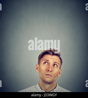 Headshot confused man thinking looking up isolated on gray wall background with copy space above head. Human face expressions, emotions, feelings, bod Stock Photo