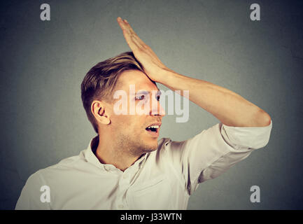 Regrets wrong doing. Closeup portrait silly young man, slapping hand on head having a duh moment isolated on gray background. Negative human emotion f Stock Photo