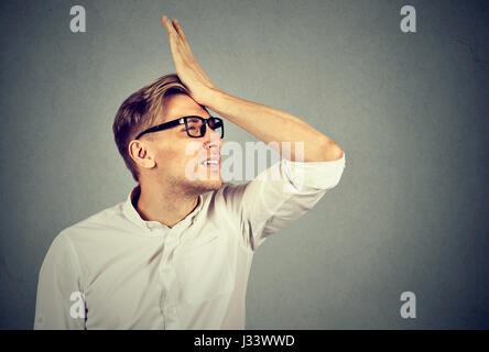 Regrets wrong doing. Silly young man in glasses slapping hand on head having a duh moment. Negative human emotion facial expression feeling, reaction Stock Photo