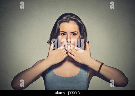 Closeup portrait of young woman covering with hands her mouth isolated on gray wall background Stock Photo