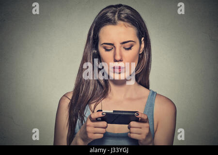 Portrait young angry woman unhappy, annoyed by something, someone on her cell phone texting, receiving bad sms text message news isolated gray wall ba Stock Photo