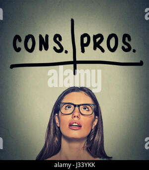 pros and cons, for and against argument concept. Young business woman with glasses looking up deciding isolated on gray wall background. Face expressi Stock Photo