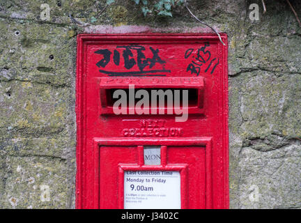 a view of black graffiti on a pill post letter box in a stone wall Stock Photo