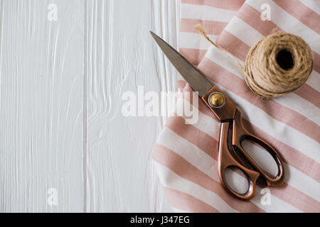 Beautiful scissors, striped fabric and twine spool on a white tabletop board with copyspace Stock Photo