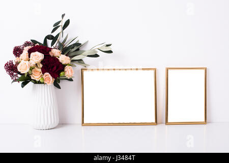 Two golden frames mock-up on white wall background, home decor with flowers Stock Photo