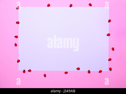 White sheet of paper on a pink surface, around decorative wooden ladybugs Stock Photo