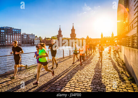 Group of female and male young runners jogging outside in golden evening light at sunset in summer with retro vintage style toned filter effect Stock Photo