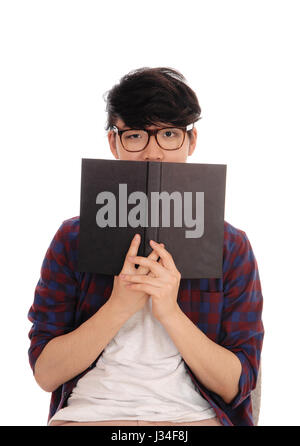 A young Asian man standing in a checkered shirt and glasses, holding a book in front of his face, isolated for white background. Stock Photo
