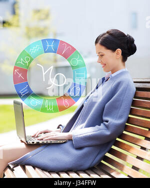 smiling woman with laptop and zodiac signs in city Stock Photo