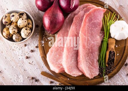 Horizontal photo with few slices of raw pork meat on wooden plate with spice as pepper or paprika around together with vegetable and quail eggs in bow Stock Photo
