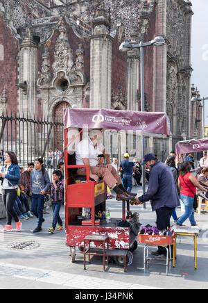Zocalo, Mexico City, Mexico -23 April 2017: Shoeshine man, client, & passersby at one of the many shoeshine stands in front of the Cathedral Stock Photo