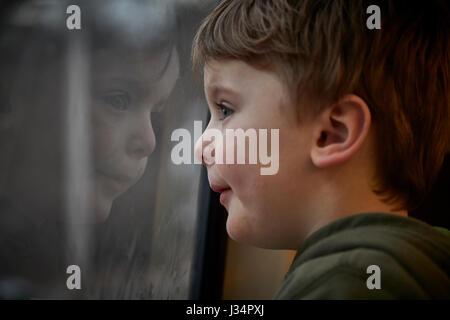 Boy on a train staring out of the window with his face reflecting in the coach window Stock Photo