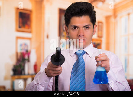 Handsome young Man cleaning home with vacuum cleaner with a Disinfectant spray in his other hand Stock Photo