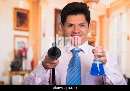 Handsome young Man cleaning home with vacuum cleaner with a Disinfectant spray in his other hand Stock Photo