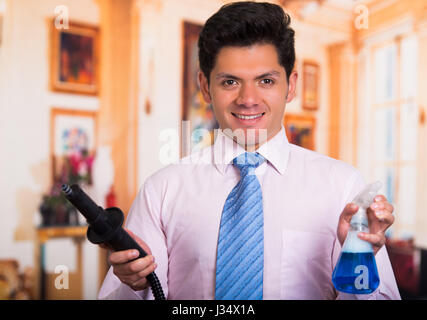 Handsome young Man cleaning home with vacuum cleaner with a Disinfectant spray in his other hand Stock Photo