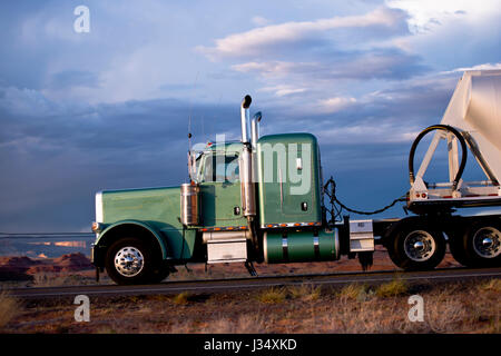 Super classic green big rig semi truck with bulk semi trailer on the road against the blue sky Stock Photo