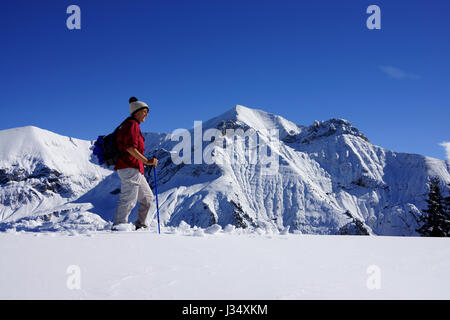 Woman hiking on snowshoes in fresh snow on Standfluh with Mt. Dreispitz in back, Bernese alps, Kiental, Switzerland Stock Photo