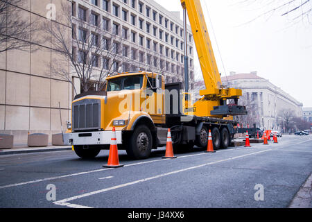 Powerful yellow big rig semi truck with mounted on the chassis a crane with a sliding boom fenced by orange road work marking posts for the attention  Stock Photo