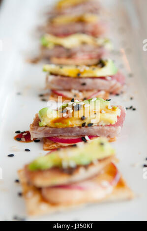 Closeup of ahi tuna appetizer, with avocado and radish on crackers, served on a white plate Stock Photo