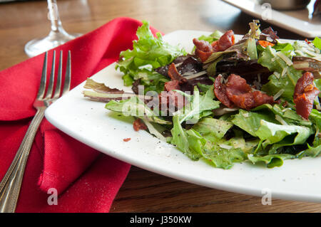 Close up of a mixed greens salad with crispy bacon, parmesan cheese, and cracked black pepper, in a restaurant setting Stock Photo