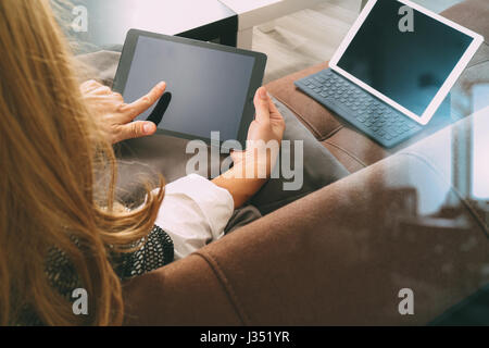 brunette woman using digital talet and laptop computer on sofa in living room Stock Photo